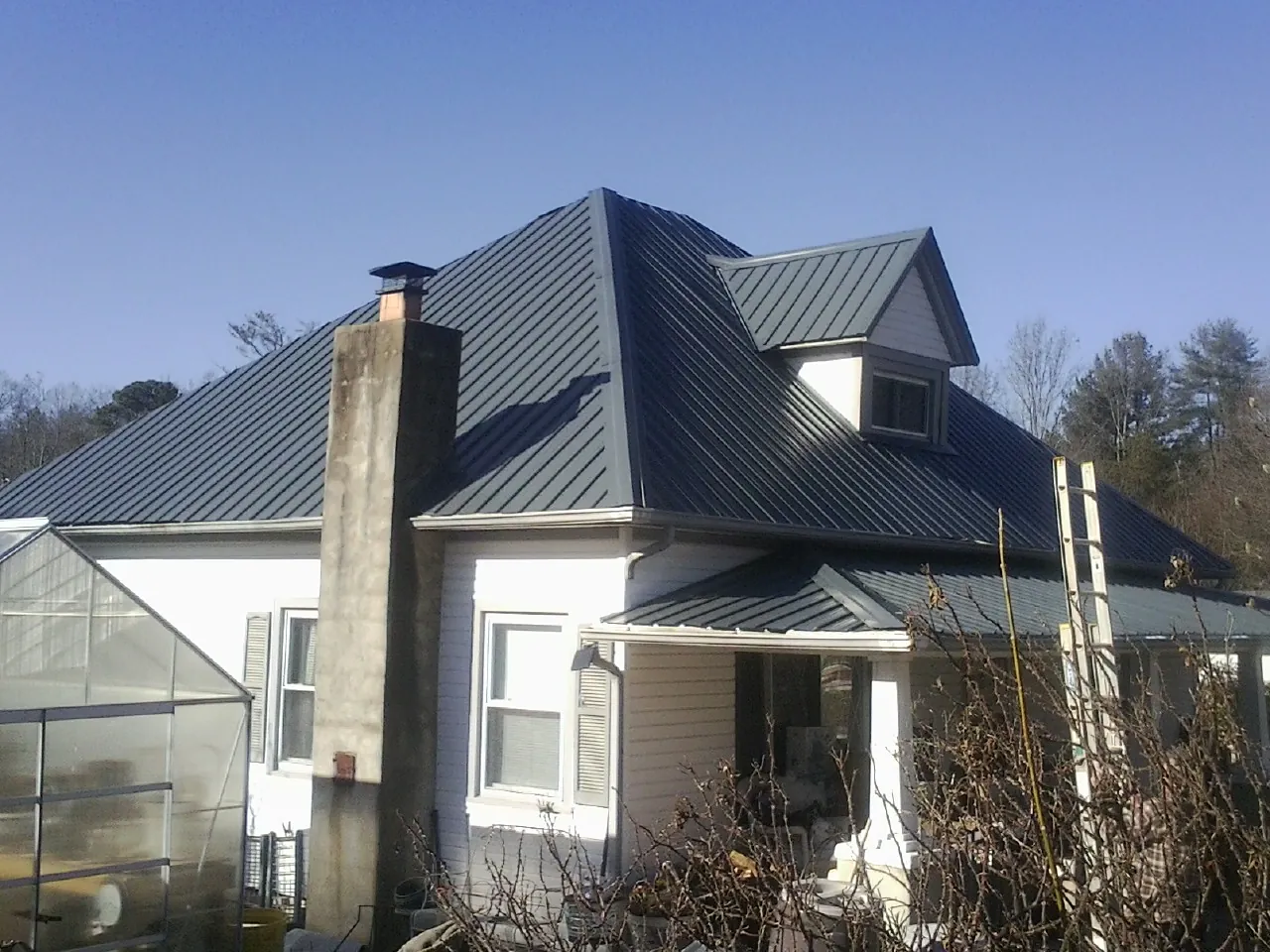 Dark blue standing seam metal roof on a white farmhouse with dormer — Slate & Tile Roof Repair by Roofing Brothers in Lake Charles