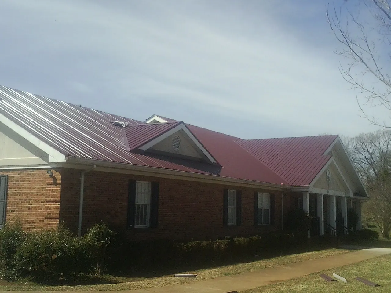 Red metal roof with gabled entries on a long brick building, from a Hail Damage Roof Repair job in Lake Charles