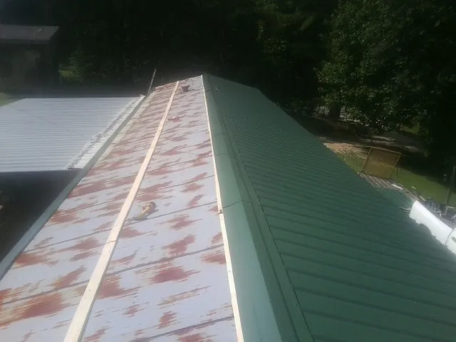 Old rusted panels beside newly installed green metal roofing — Wind Damage Roof Repair by Roofing Brothers in Lake Charles