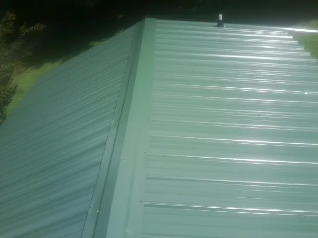 New green metal panels meeting at the ridge of a roof — Flat Roof Repair work by our crew in Lake Charles