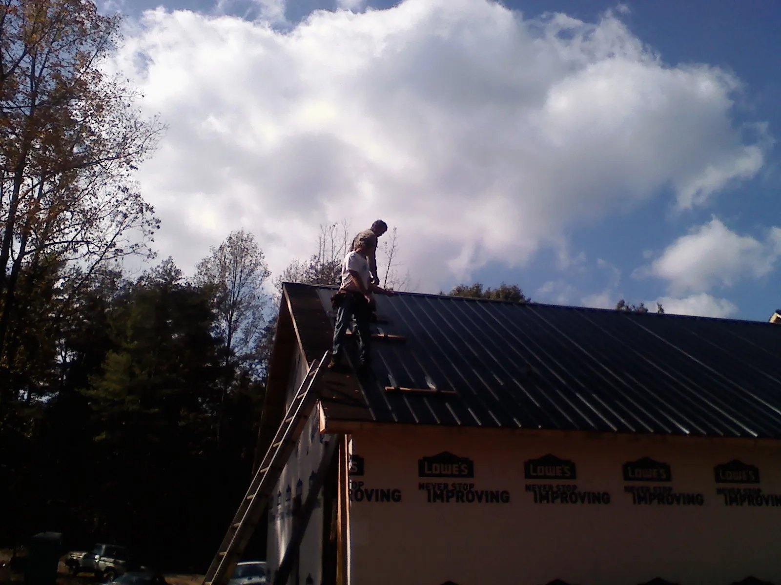 Roofer fastening dark metal panels high against a cloudy sky, from a Roof Inspection job in Lake Charles