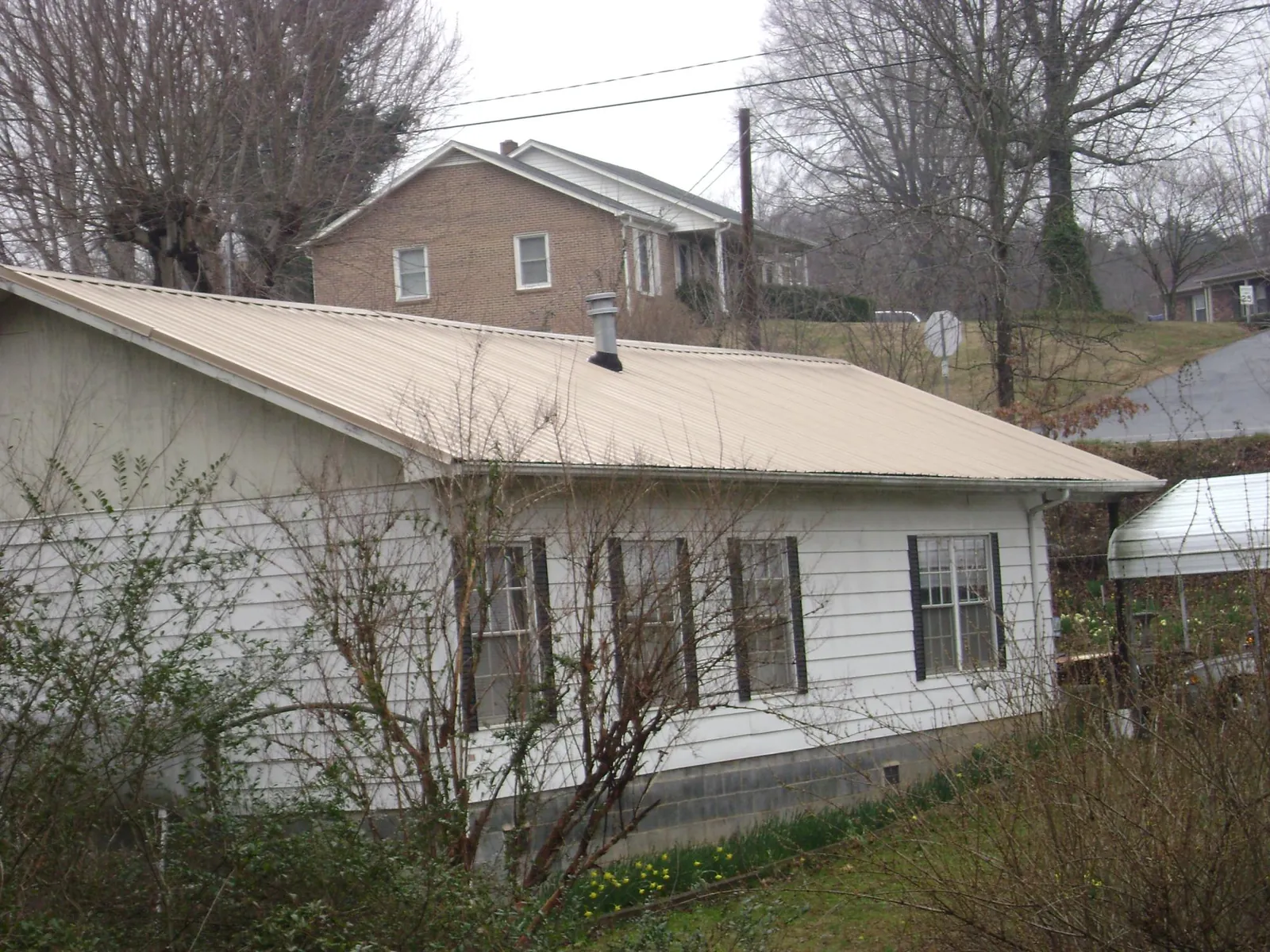 Tan metal roof on a white sided house set into a hillside — Commercial Roofing by Roofing Brothers in Lake Charles