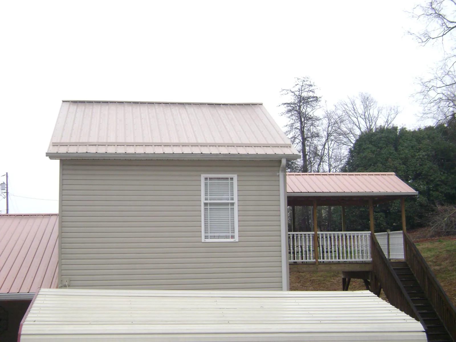 Tan metal roofs on a two story addition and attached porch, from a Roof Replacement job in Lake Charles